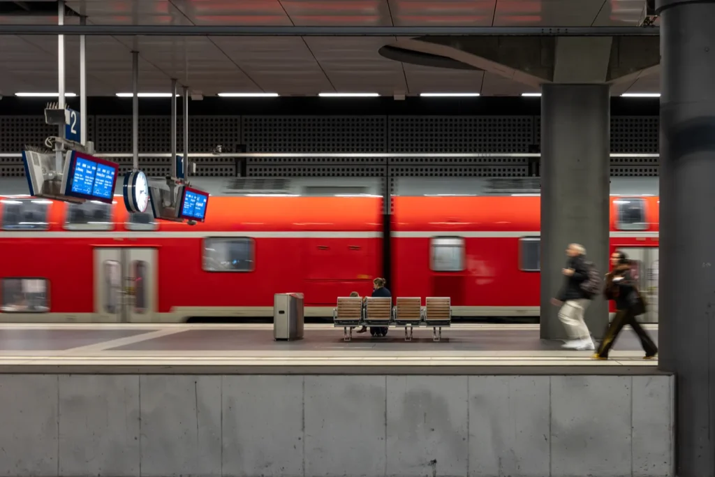 Treno suburbano rosso in stazione con passeggeri in attesa